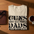 Cream t-shirt with "Guns don't kill people Dads with b*tches do" text.