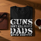 Black t-shirt with "GUNS DON'T KILL PEOPLE DADS WITH PRETTY DAUGHTERS DO" text.
