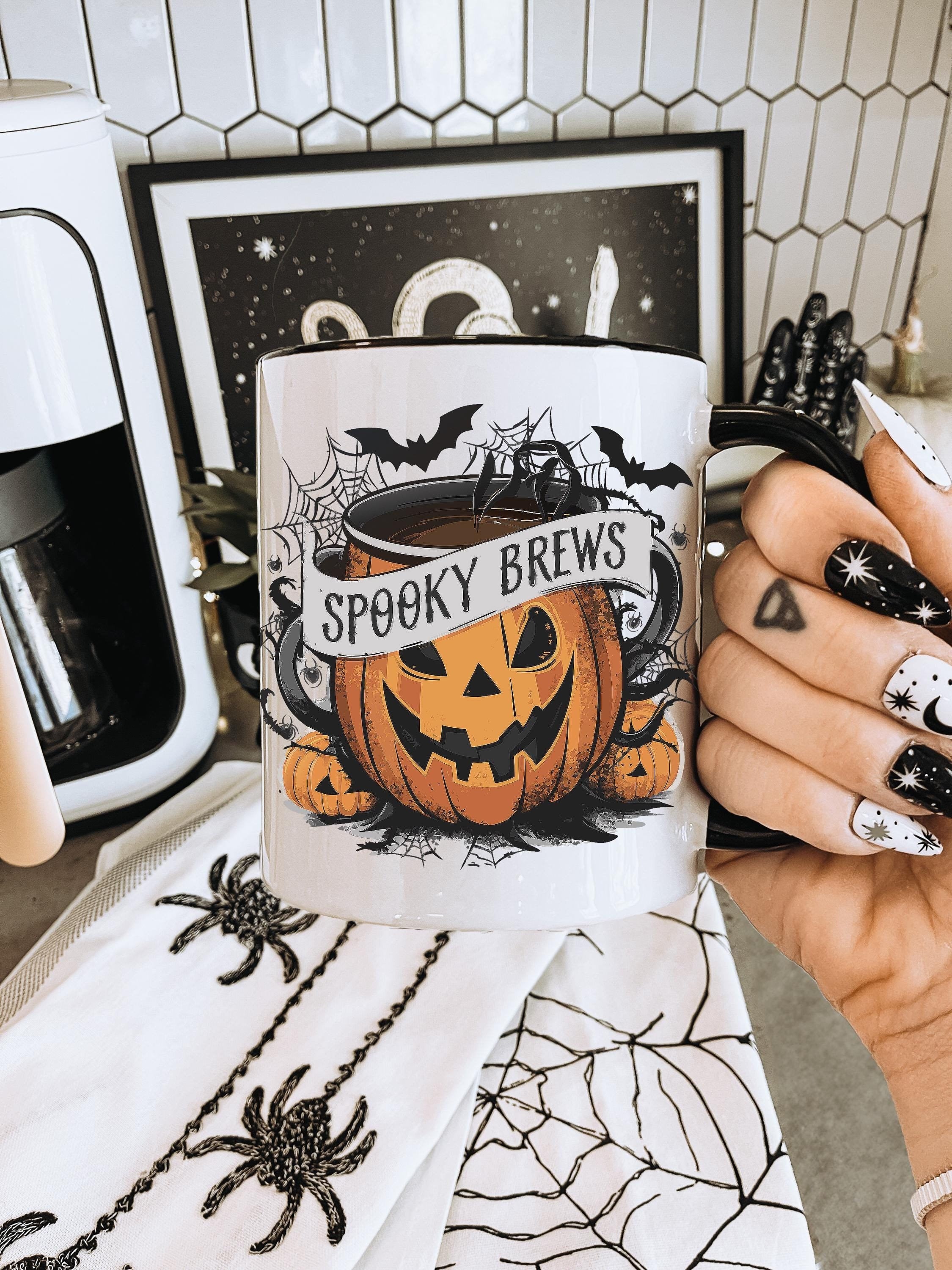 White ceramic mug with 'Spooky Brews' text, featuring a pumpkin jack-o'-lantern, bats, and cobwebs design. Perfect for Halloween decor and fall beverages.